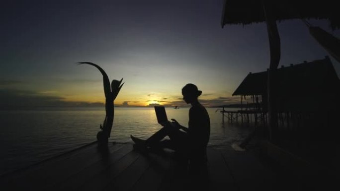 日落时在甲板上的笔记本电脑上工作的年轻女子