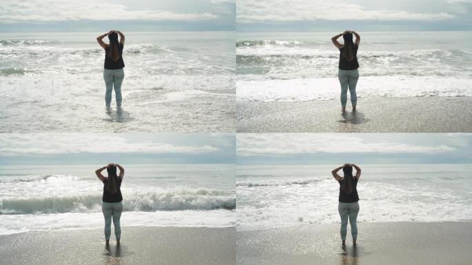 风雨如磐的大海和云朵，一个丰满的年轻女子站在沙滩上，用手托着她的头，海浪打在我的腿上。