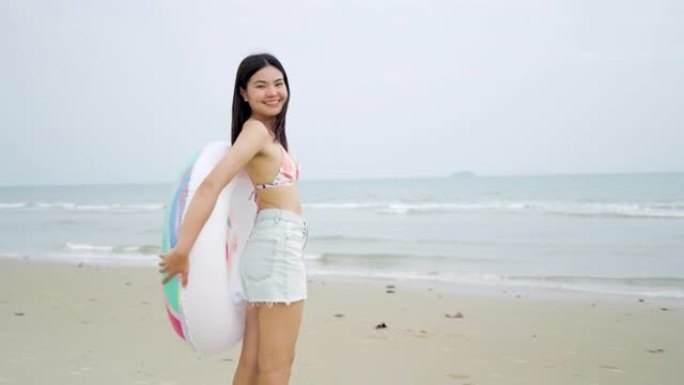 在海滩上跑步的亚洲女孩在白天的晚上使用充气戒指。