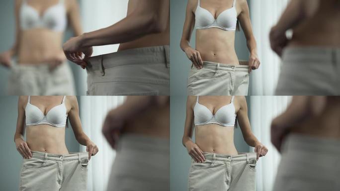 穿着大裤子的苗条女人在镜子前摆姿势，节食，减肥