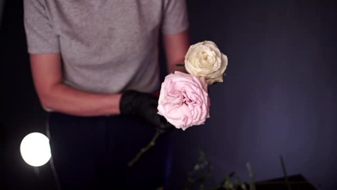 花店收集了一束牡丹，白色和粉红色的玫瑰。花匠戴着黑色防护手套的手的特写镜头。花店创造了一束美丽的花束