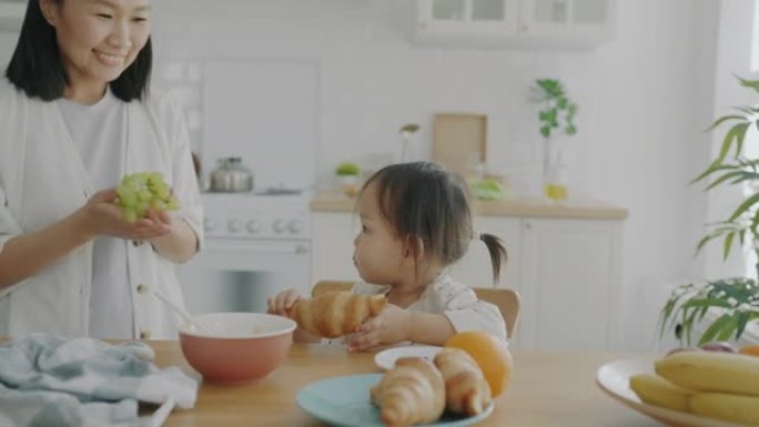可爱的孩子吃羊角面包的慢动作肖像慈母在家厨房里带葡萄时