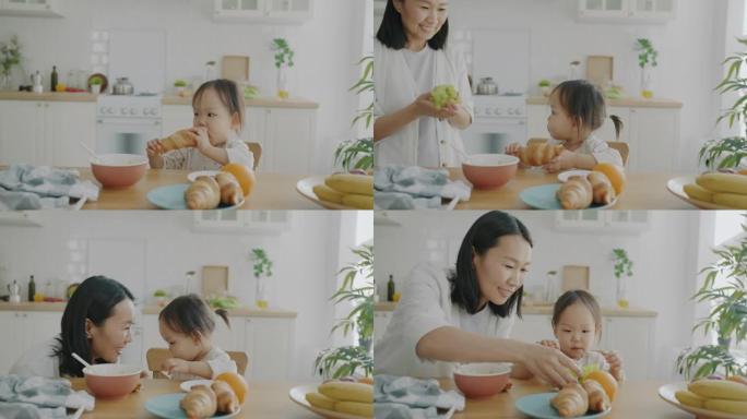 可爱的孩子吃羊角面包的慢动作肖像慈母在家厨房里带葡萄时