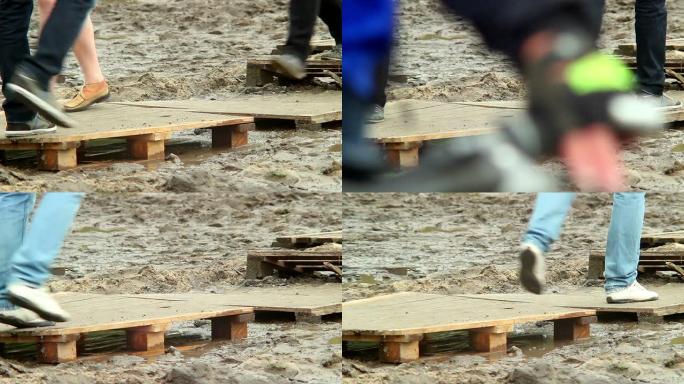 人们踩在木制平台上，走过肮脏的地方