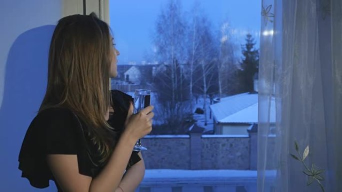 怀着白葡萄酒的梦想女孩坐在窗台上，享受冬天的夜晚