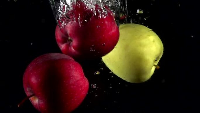 慢动作红色和黄色苹果落在黑色背景上的水中。美丽的新鲜水果在水族馆里飞溅。有机水果，健康食品，饮食，概