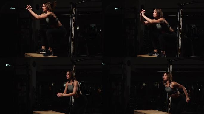 美丽的女性健身运动员表演盒子跳在一个黑暗的健身房穿着黑色运动上衣和短袜与脸部隐藏