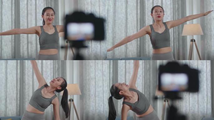 年轻的亚洲教练女性穿着运动服对着镜头说话，一边伸展身体，一边在家记录教学锻炼