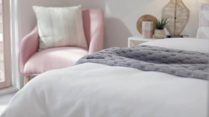 漂亮的卧室里有一把舒适的粉色椅子，早晨的阳光透过窗户流到柔软舒适的床上，床上铺着绗缝毯子。