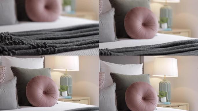 柔软舒适的床上装饰枕头和靠垫，配有装饰灯，将柔和的光线投射到床头柜上的小花瓶上。