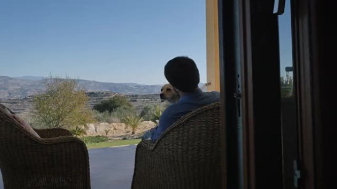 一个男人带着狗在现代别墅的露台上休息
