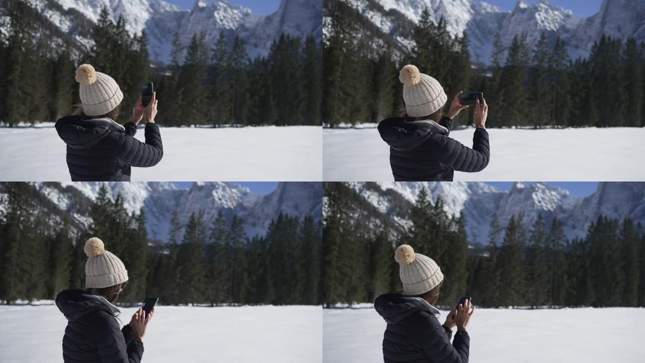 年轻女子冬季在山区用手机拍照