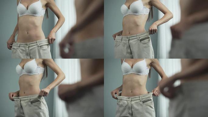 穿着大裤子的运动女性在镜子附近摆姿势，节食的结果