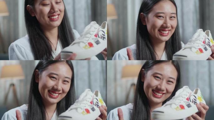 微笑的亚洲女鞋设计师拿着彩色图案运动鞋的特写镜头，向相机展示竖起大拇指的手势