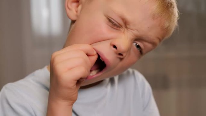 一个小男孩用手在嘴里摇动婴儿牙齿的特写镜头。