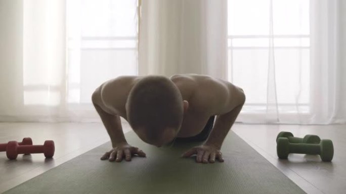 4K男人在家里锻炼，在瑜伽垫上做俯卧撑，旁边有哑铃。运动，运动，健康生活理念。