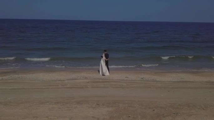 穿着婚纱的新娘和新郎沿着海边散步，拥抱，亲吻，奔跑，享受自己。鸟瞰的航空摄影。夫妻正在度假的酒店拍摄