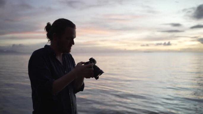 一名男子在日落时在海滩拍照的剪影