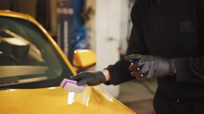 年轻人，汽车抛光服务人员抛光汽车发动机罩，用纳米陶瓷成分或蜡抛光黄色豪华跑车。汽车细节。抛光工具。