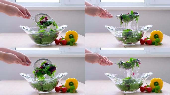 超级慢动作拍摄五颜六色的蔬菜和水滴的飞刀女人用筛子在玻璃盘中清洗沙拉，将其提起，在周围泼水