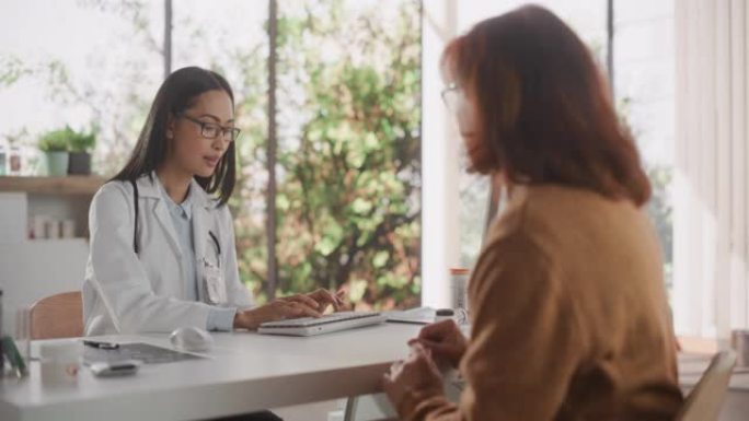 年轻的亚洲医生正在为一名成年女性患者开药，并在健康诊所咨询期间听取她的反馈。穿着实验室外套的医生坐在