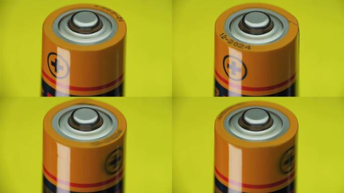 碱性电池在黄色背景上旋转。加号是特写