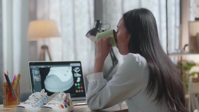亚洲女鞋设计师在家里的笔记本电脑上一边喝着咖啡一边设计鞋子。制鞋程序概念