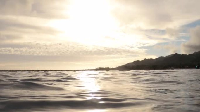在南太平洋拉罗汤加库克群岛阿瓦鲁阿区海滨海湾海岸线的平静海浪海水表面上方，手握美丽的金色日落云