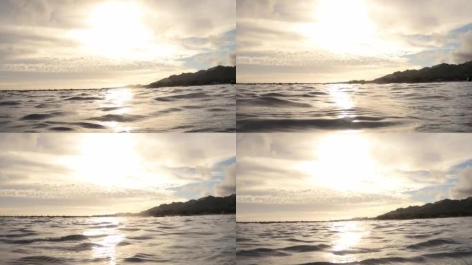 在南太平洋拉罗汤加库克群岛阿瓦鲁阿区海滨海湾海岸线的平静海浪海水表面上方，手握美丽的金色日落云