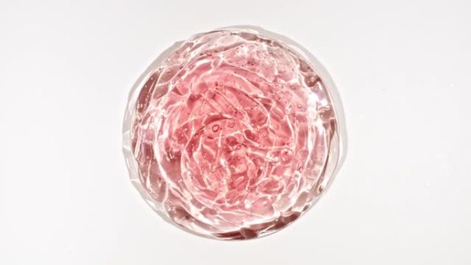 在Petri玻璃碗中带有气泡的透明红色化妆品凝胶液的旋转。宏丸血清、乳膏、透明质酸。有机化妆品，药品