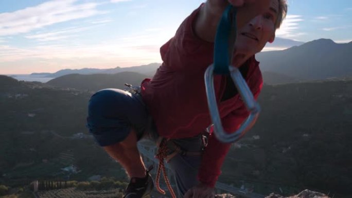 成熟的男性攀岩者登上陡峭的脸，夹子保护