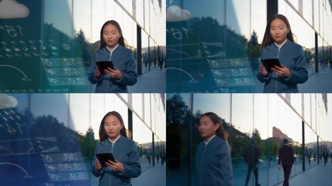 年轻的亚洲女企业家在沿着现代商业大楼行走时在数字平板电脑上检查天气应用程序