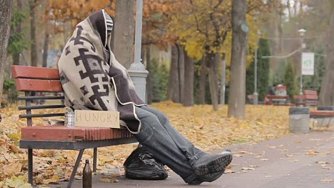 绝望的无家可归者坐在长凳上，饥饿的人乞求慈善