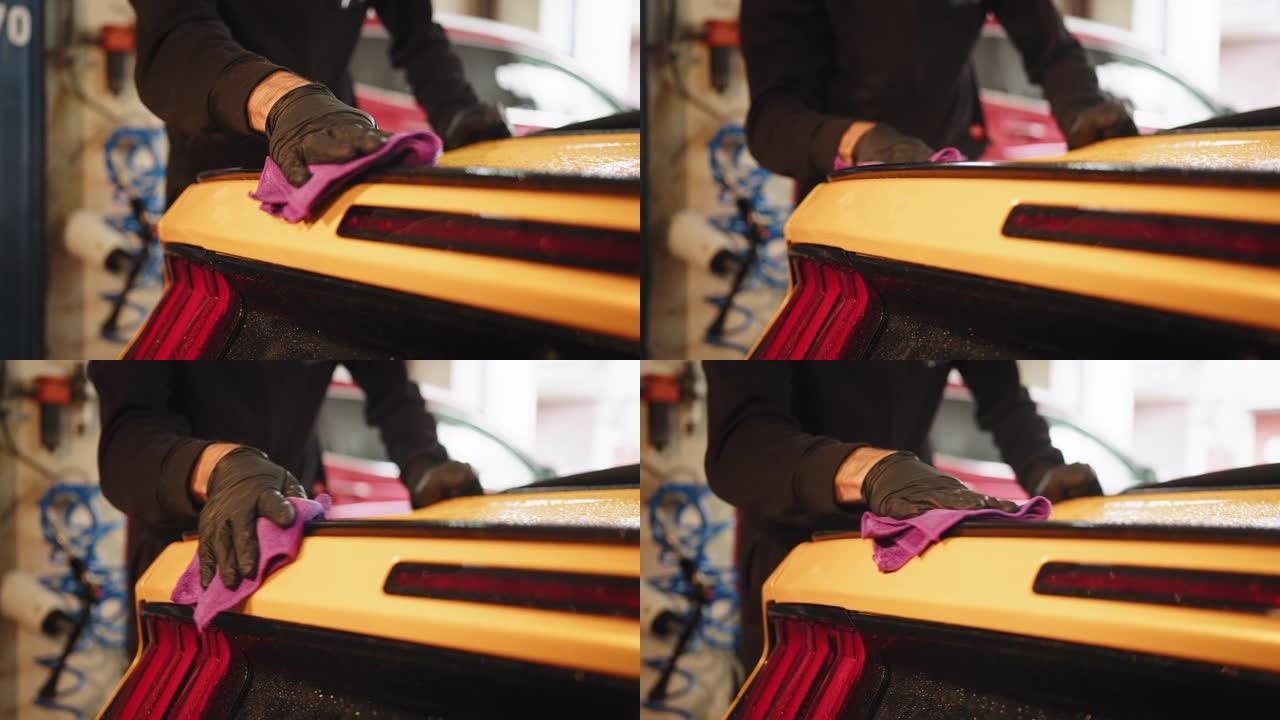 男性洗车工手的裁剪视图握着超细纤维，在车辆尾灯下擦亮黄色运动型豪华车。汽车细节和清洁概念。男性洗车工