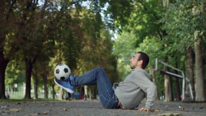 户外动作镜头，职业足球运动员用球表演自由式技巧。自信的年轻足球运动员在公园的夏日里炫耀杂耍技巧