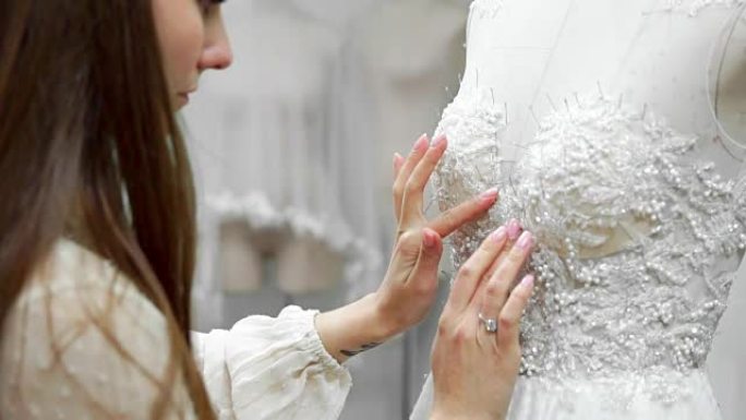一个女孩的肖像通过独家订购在穿着人体模型的连衣裙上缝制织物和水钻来制作婚纱。婚纱的生产。小生意