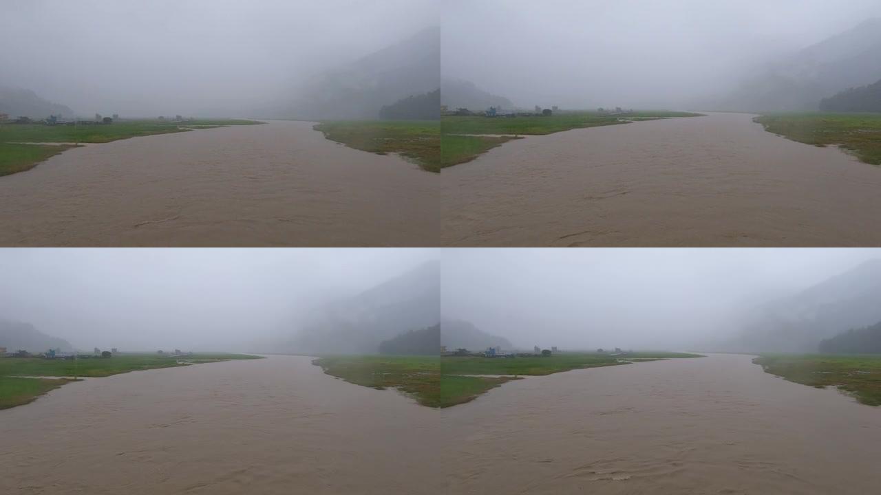 在尼泊尔季风期间，在大雨中站在桥上观看洪水泛滥的河流。