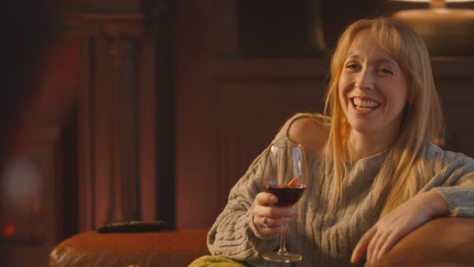 两个女性朋友在休息室的沙发上放松和大笑，用舒适的火拿着一杯酒