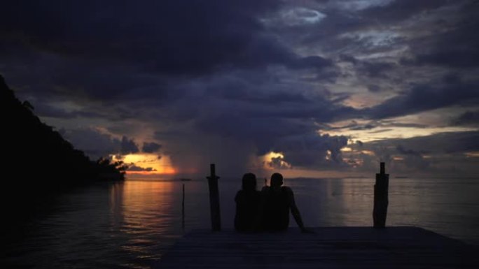 年轻夫妇坐在码头上享受热带日落