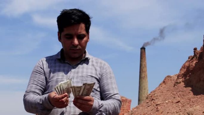 一名印度男子站在砖厂附近时数着500卢比的钞票-月薪，生意，利润，印度货币