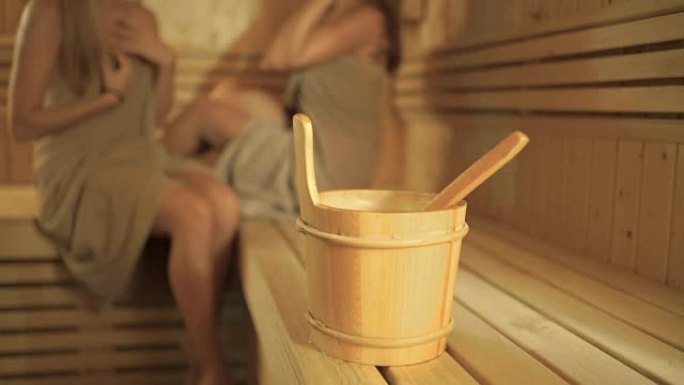 两个女孩背景下的桑拿浴室里有勺子的木桶