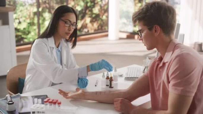 年轻的亚洲过敏症专家正在进行点刺划痕测试，以在医疗诊所进行健康检查时诊断年轻男性前臂的任何过敏反应。