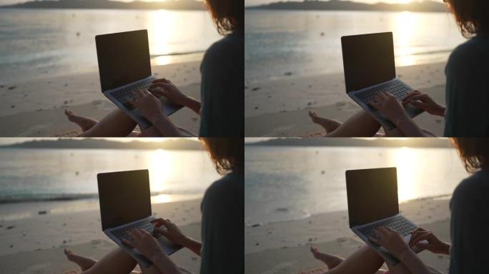 日落时，一名年轻女子在海滩上的笔记本电脑上工作的特写镜头