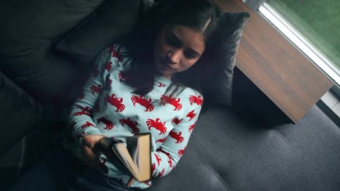 一名年轻女子躺在家里的沙发上读圣经。合上书，心情平和。顶视图