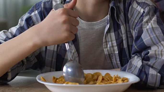 男孩不情愿地将玉米片与勺子混合，使孩子沮丧，食欲不振