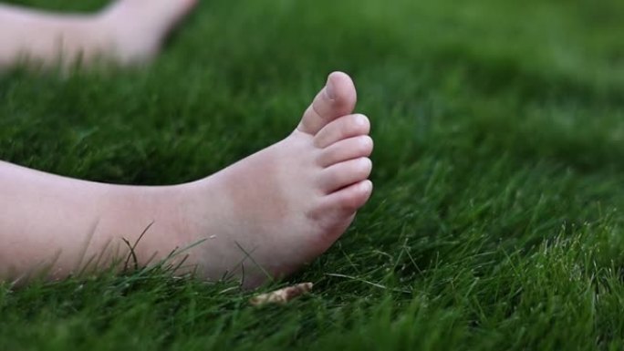 婴儿光着的小脚在绿色柔软的草地上的特写。在夏日温暖的日子里，婴儿坐在户外公园的草坪上玩耍。第一步概念