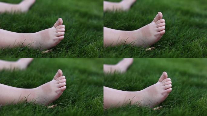 婴儿光着的小脚在绿色柔软的草地上的特写。在夏日温暖的日子里，婴儿坐在户外公园的草坪上玩耍。第一步概念