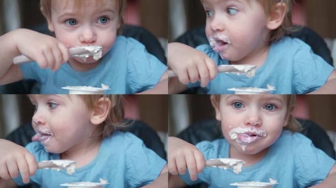 蹒跚学步的孩子坐在高脚椅上吃希腊酸奶。有趣可爱的宝宝在厨房吃饭。小女孩学习吃饭。孩子在家用硅胶勺子喂