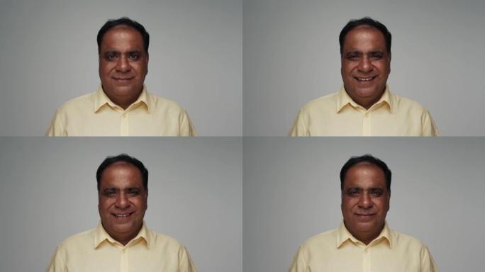 成年印度男子近距离微笑着看着相机。印度老男性的肖像被孤立在灰色背景上。彩色工作室照片中表情愉快友好的