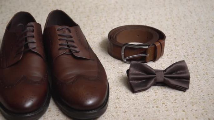 地毯上的男士婚礼棕色皮鞋。组成: 鞋子、皮带、蝴蝶。新郎早上聚会，为婚礼做准备。男鞋。